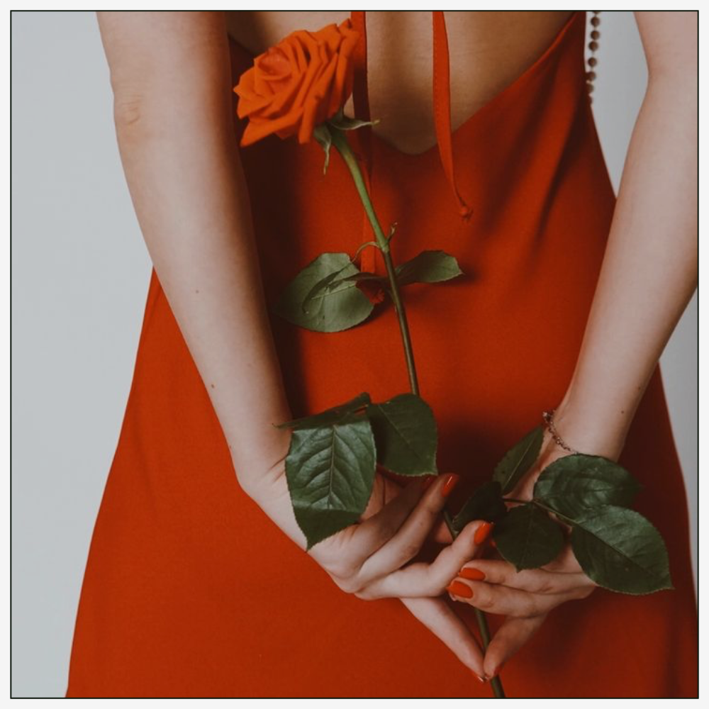 woman with red dress and nails holding a single red rose behind her back
